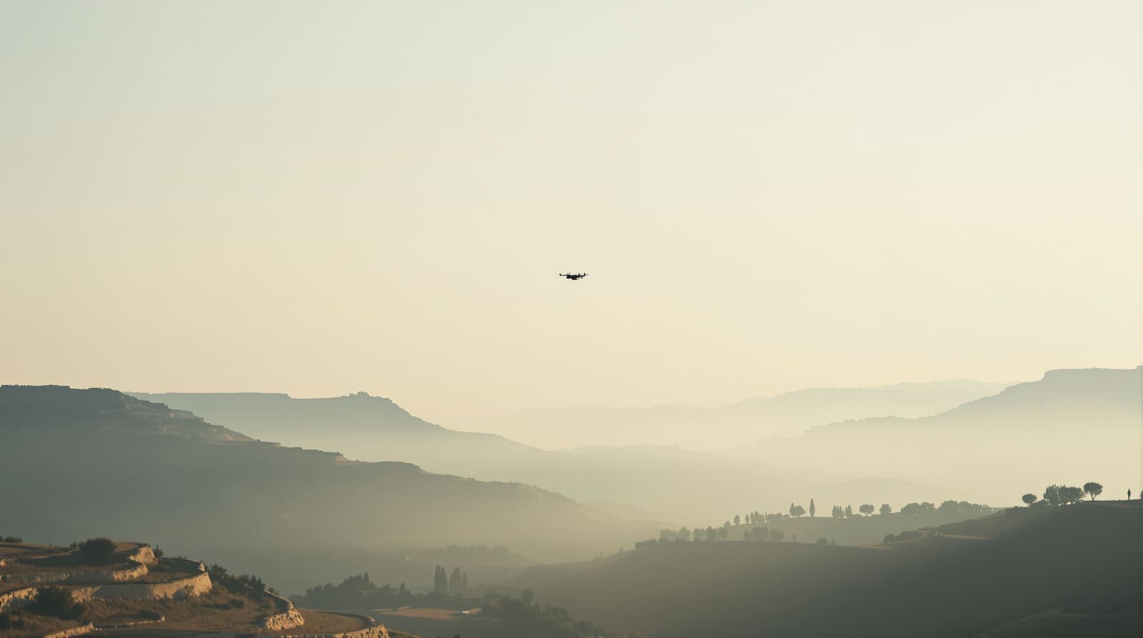 Illustration of a small drone silhouette high in a hazy dawn sky over layered scrub hills and olive terraces in southern Lebanon.
