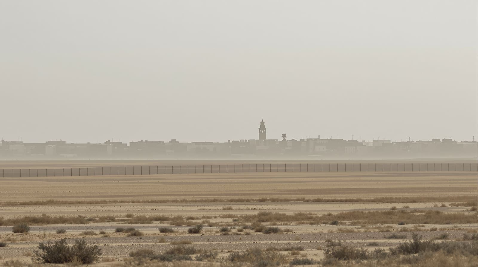 Illustration of the hazy low skyline of southern Gaza seen at dawn across flat sandy farmland and a long border fence.