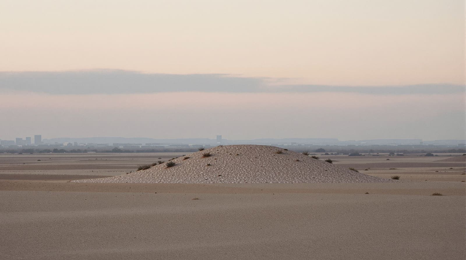 Illustration of a distant hazed skyline seen across open scrubland at dawn under soft pink cloud, viewed with a long lens.