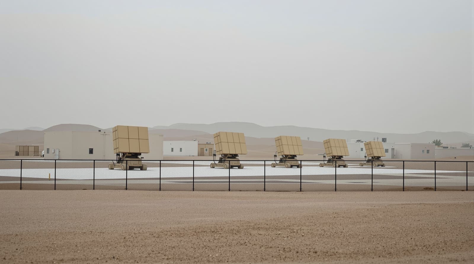 Illustration of a desert military base perimeter with air-defence launchers resting on a concrete pad at dawn