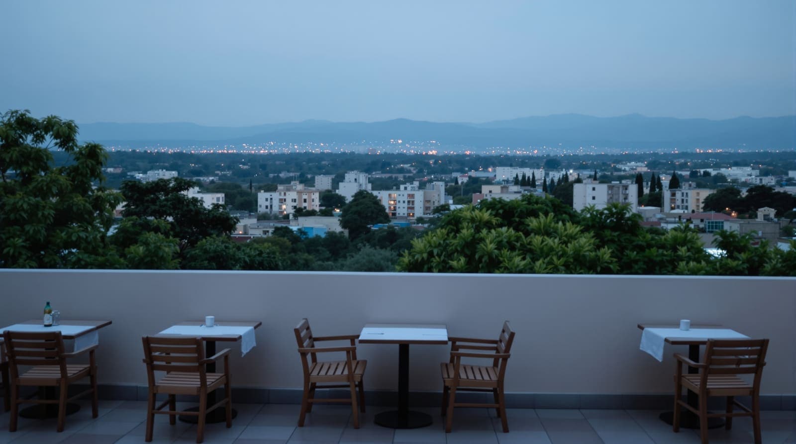 Illustration of an empty restaurant terrace overlooking the hazy Addis Ababa skyline and eucalyptus-covered hills at dusk.
