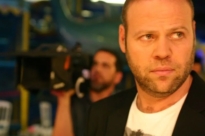 Adir Miller in close-up on a set, with a cameraman behind him