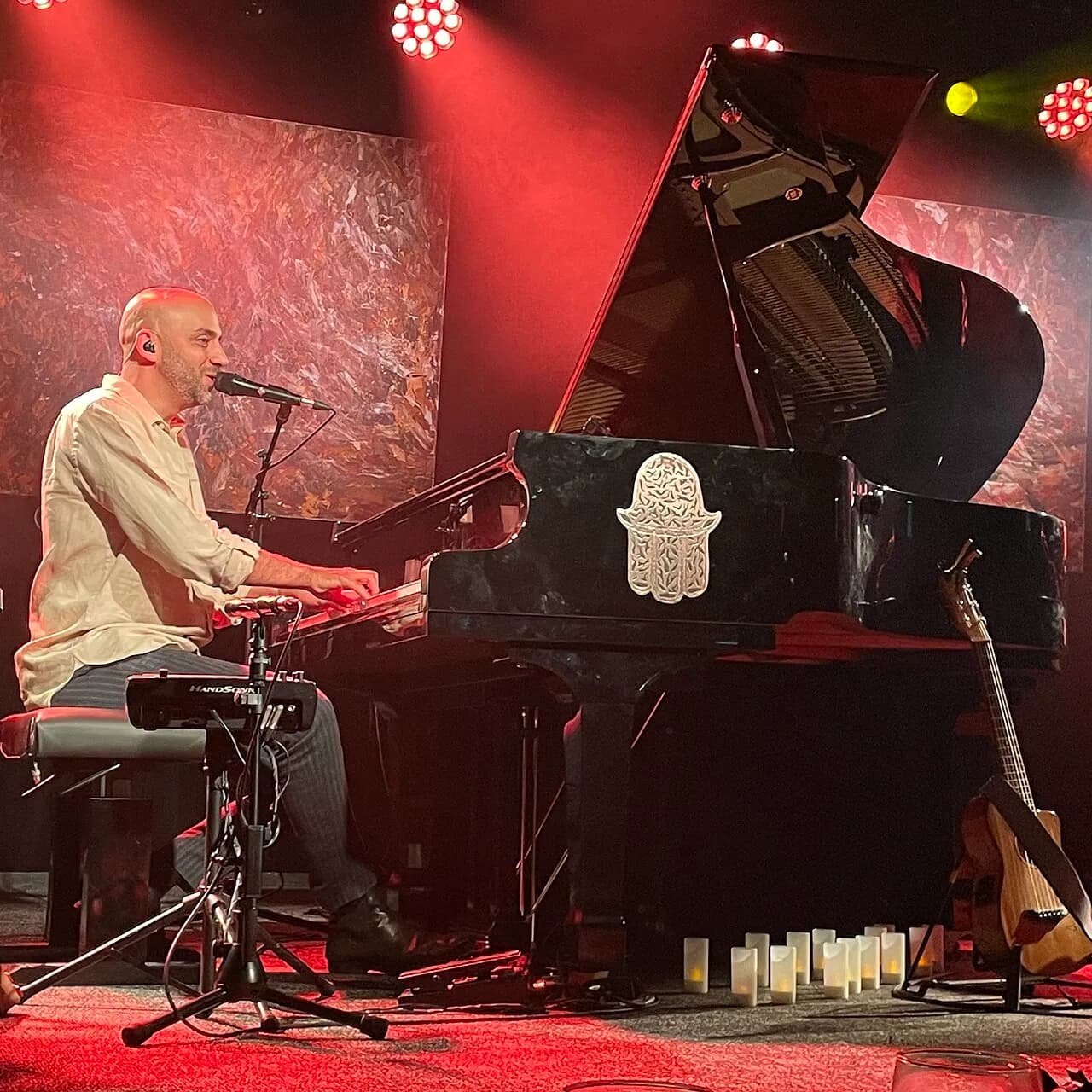 Idan Raichel singing at a grand piano under red stage lights at Zappa Tel Aviv, December 2021