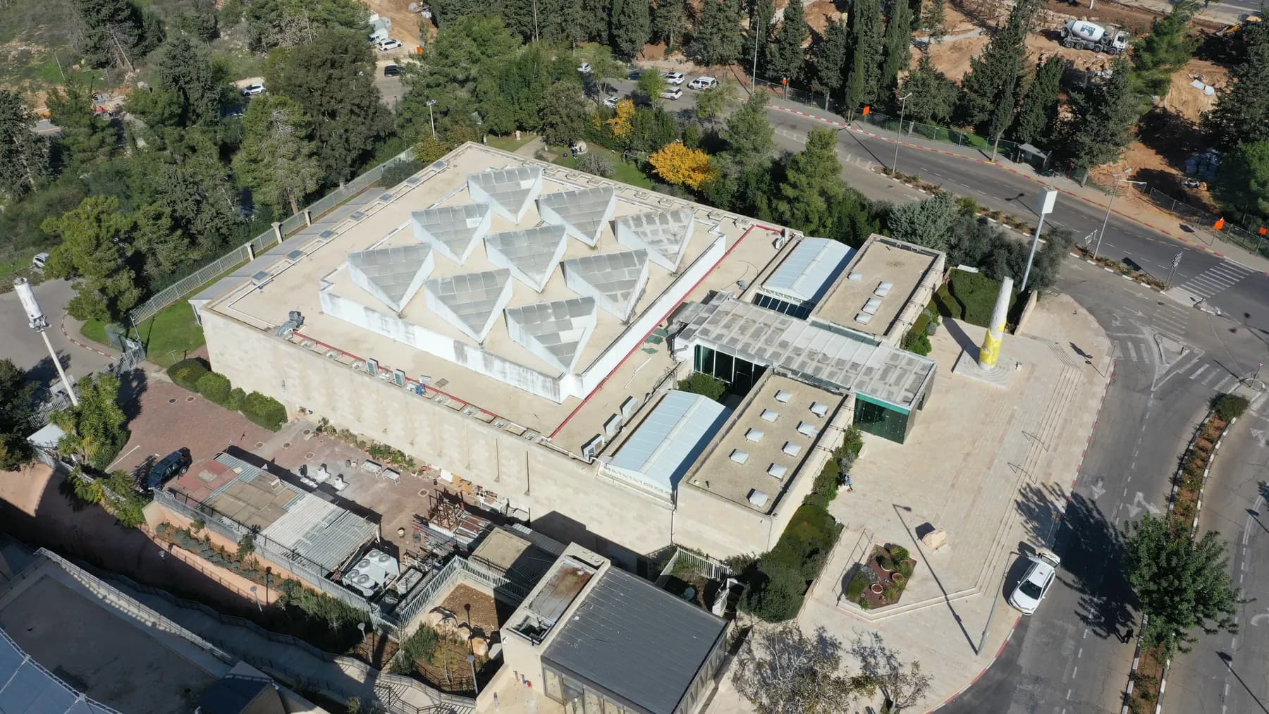 The white building of the Bible Lands Museum from above, its roof lined with pyramid skylights, among trees