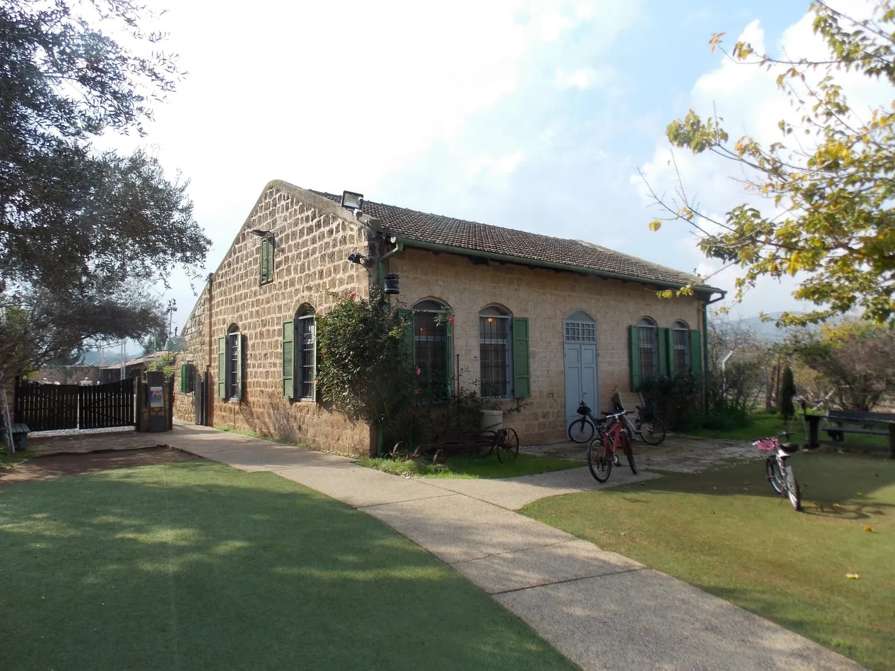 The stone farmhouse of Dubrovin Farm in Yesud HaMa'ala, with a lawn and a path in front
