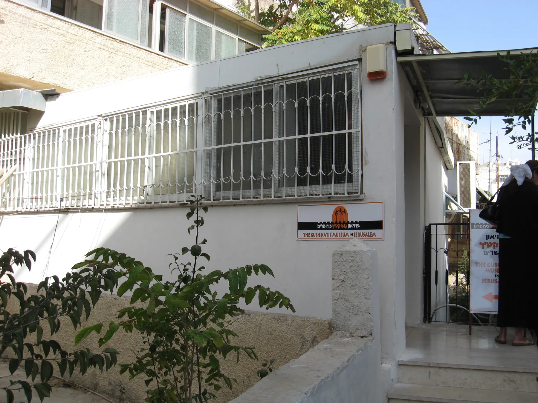 The entrance of the Gush Katif Museum, a white building with a barred window and a sign by the door