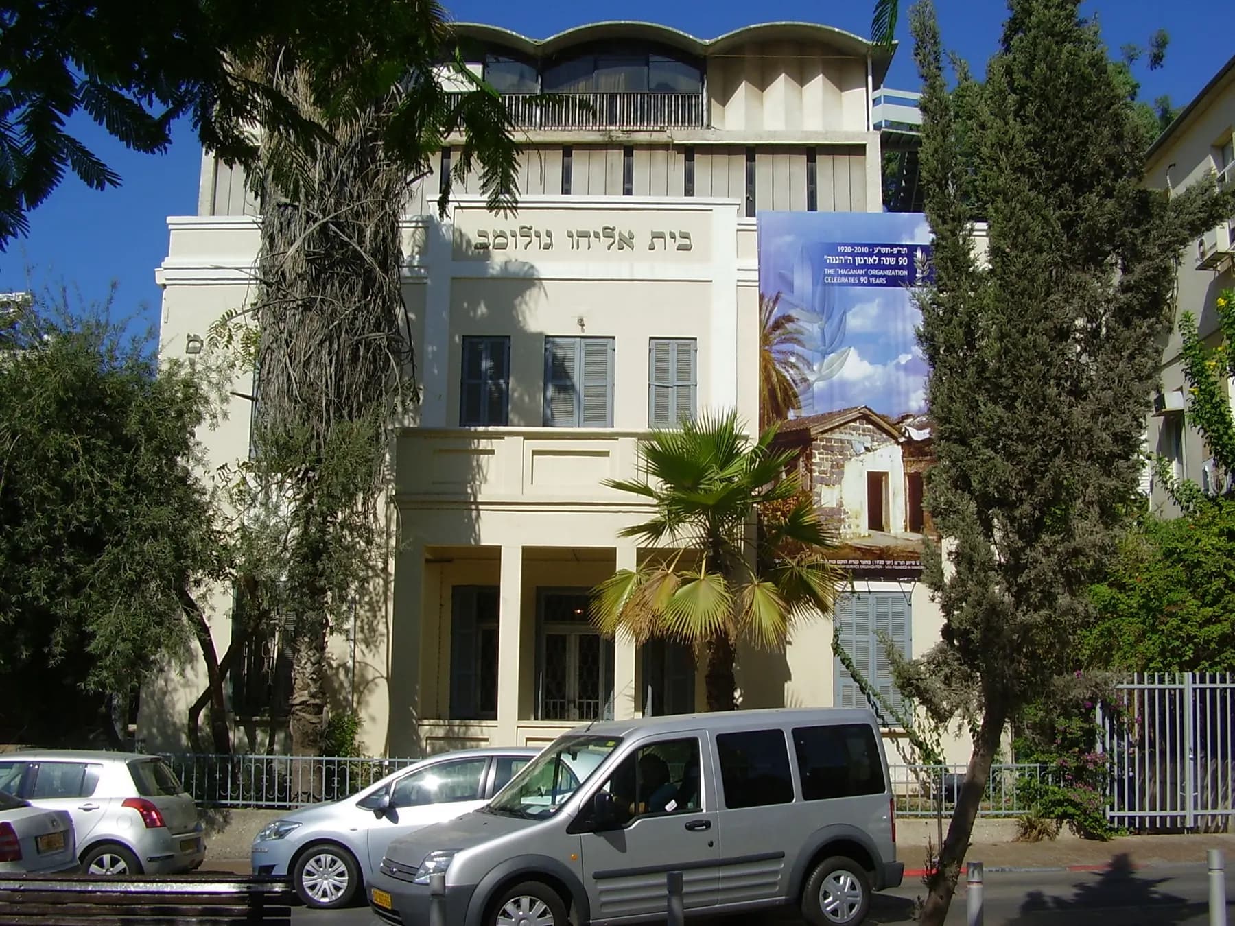 The white house of the Haganah Museum with its balconies, behind palm trees