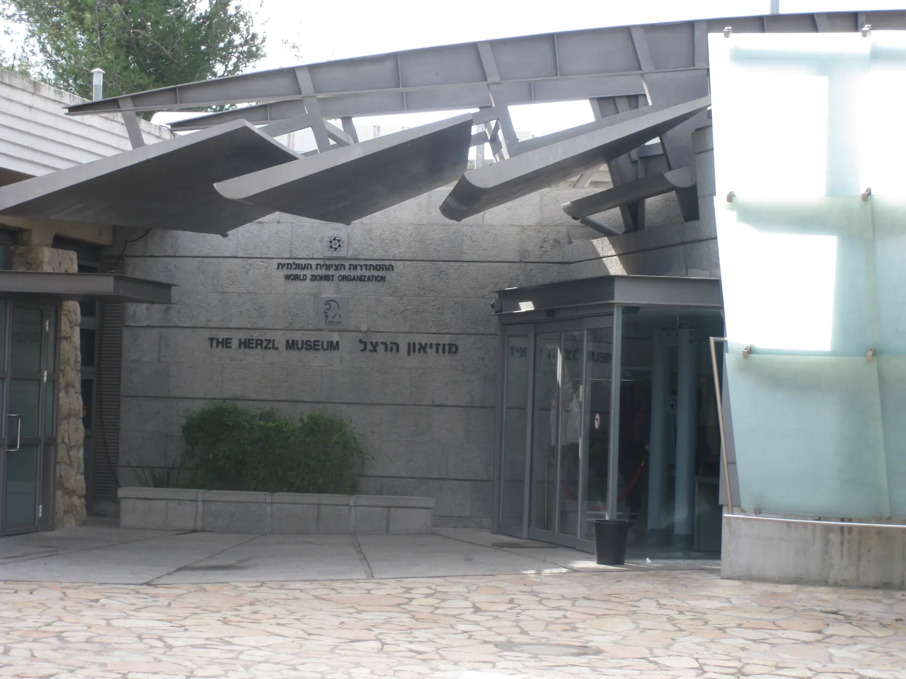 The entrance of the Herzl Museum, its name on the stone wall in Hebrew and English beside glass doors