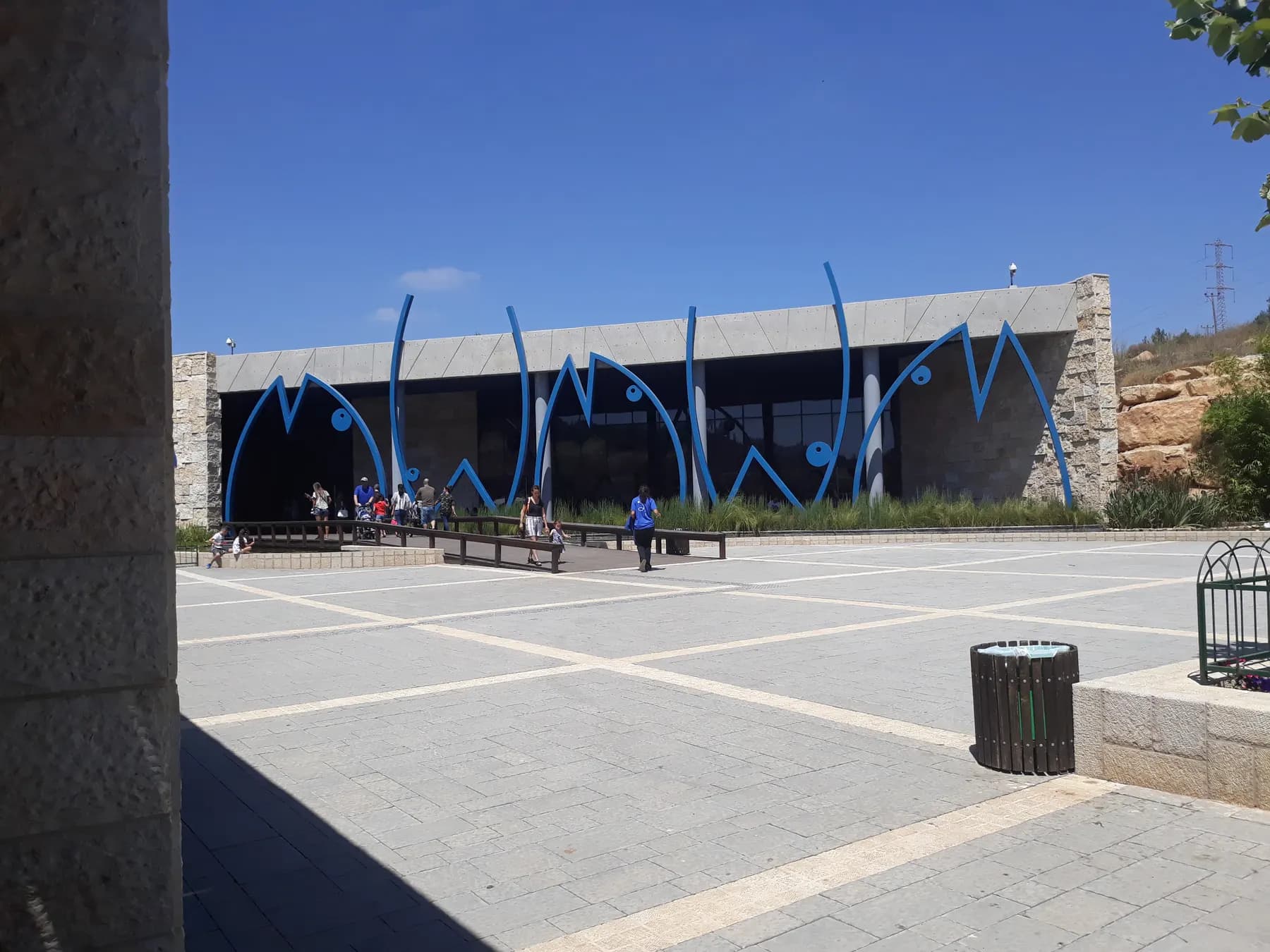 The entrance building of the Israel Aquarium, with a wave pattern along its blue front and a stone plaza before it