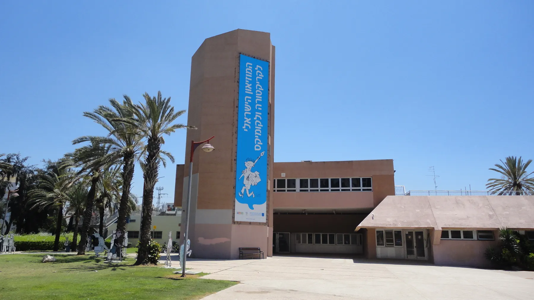 The Israeli Cartoon Museum in Holon, a low brick building beside a tower hung with a blue banner