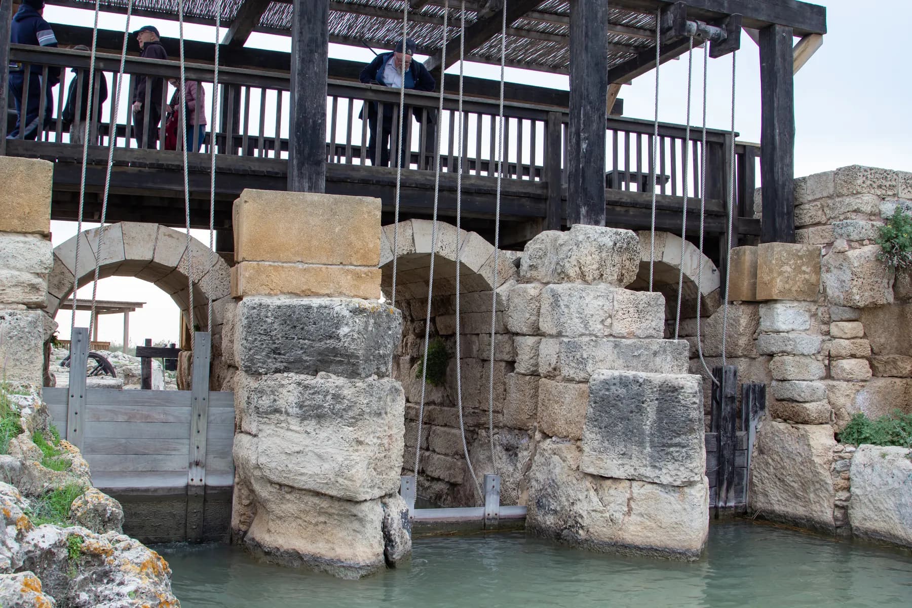 Heavy stone piers and arched sluice openings of the ancient dam at Taninim Stream, with green water passing beneath them