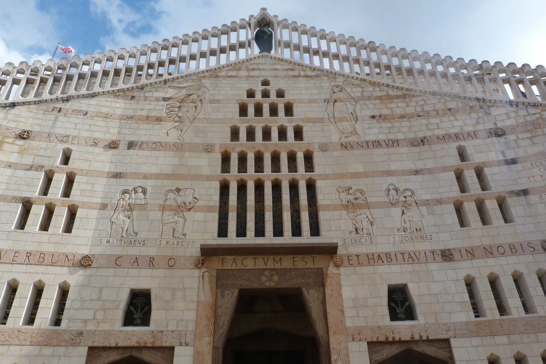 The stone west facade of the Basilica of the Annunciation in Nazareth, carved with evangelist reliefs and a Latin inscription below its colonnaded parapet