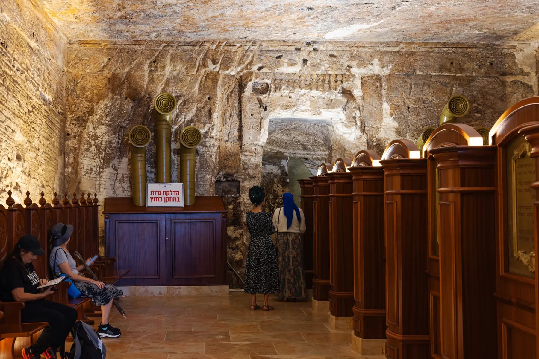 Rough rock walls and ceiling inside the cave chamber, with a wooden ark and rows of carved wooden prayer stalls set against the bare stone