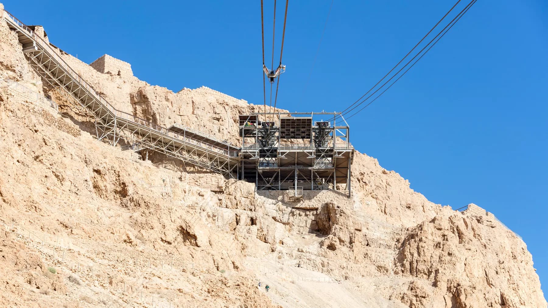The steel upper cable car station on the Masada clifftop, two haul cables running up to it against a clear blue sky