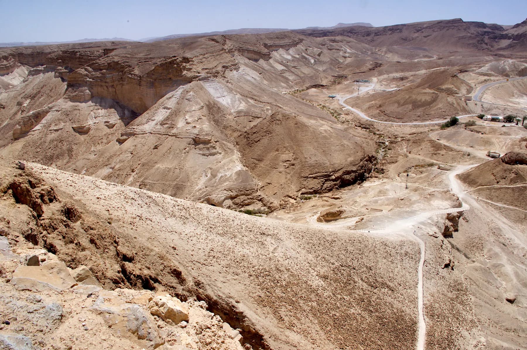 The pale gravel spur of the Roman siege ramp falling away from the summit of Masada, a footpath running along its crest down towards the desert valley and access road