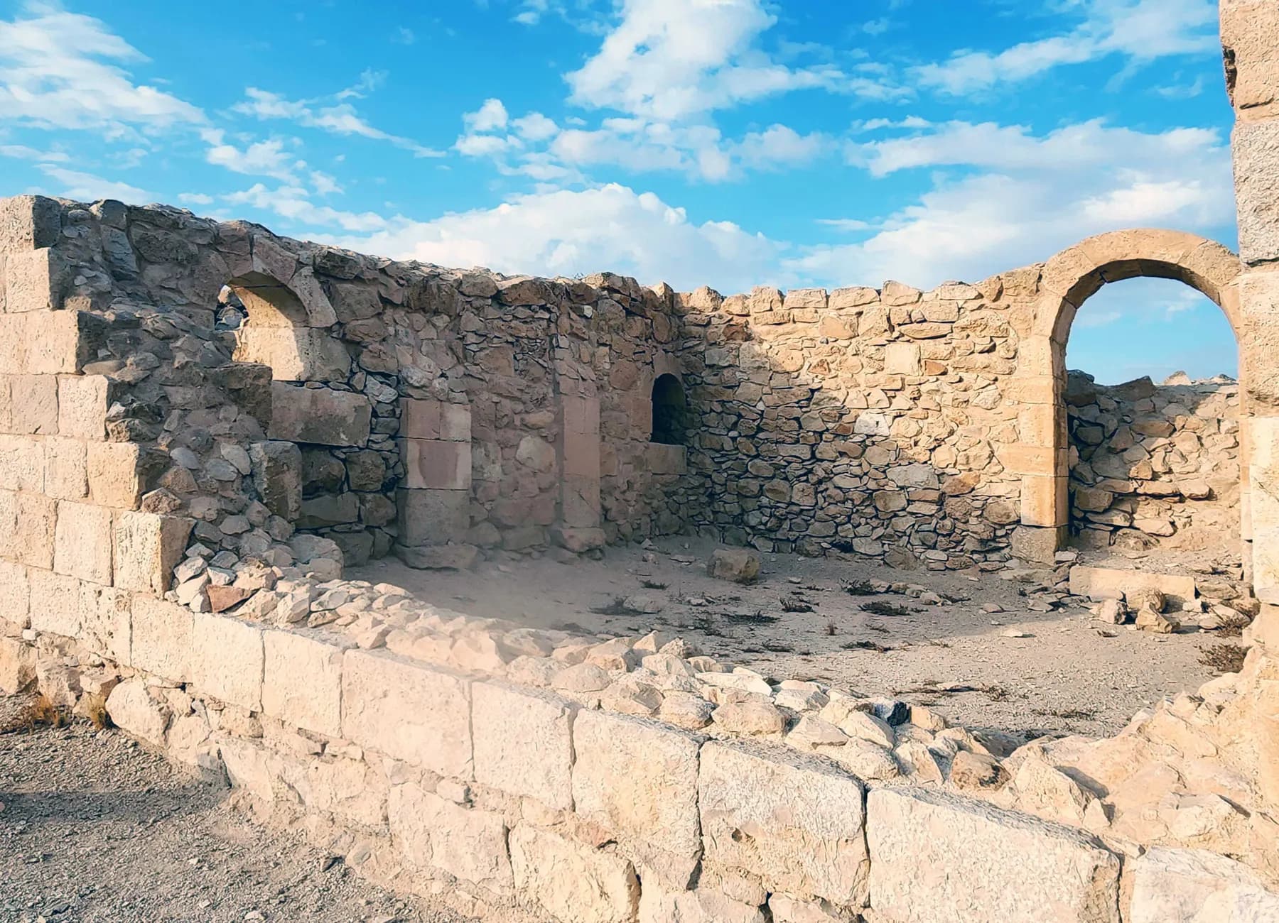 Ruined limestone walls at Avdat with an arched doorway and a smaller arched niche, standing open to a blue desert sky