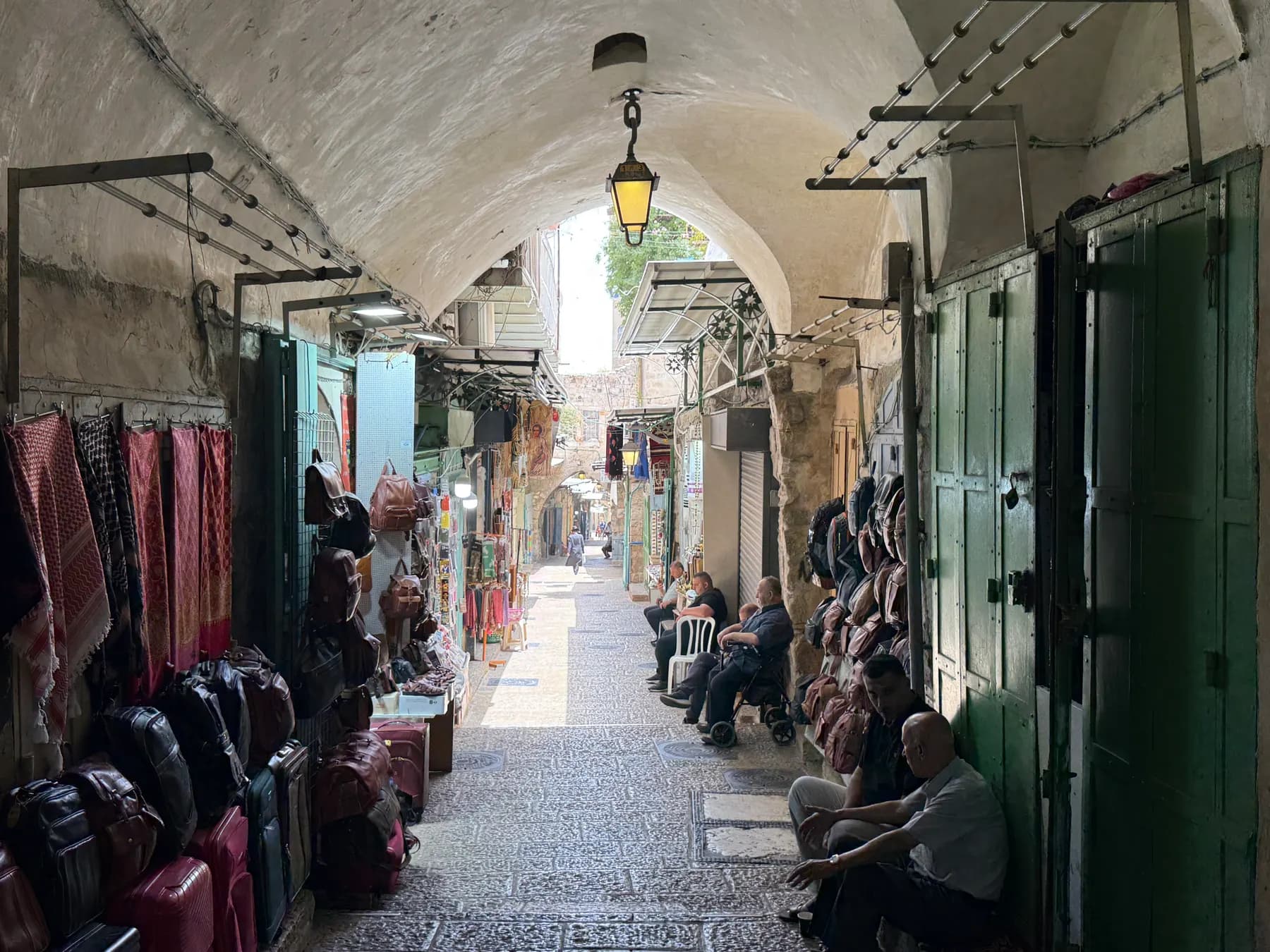 A vaulted stone lane of the Old City market, lined with stalls of scarves and leather bags beneath a hanging lantern