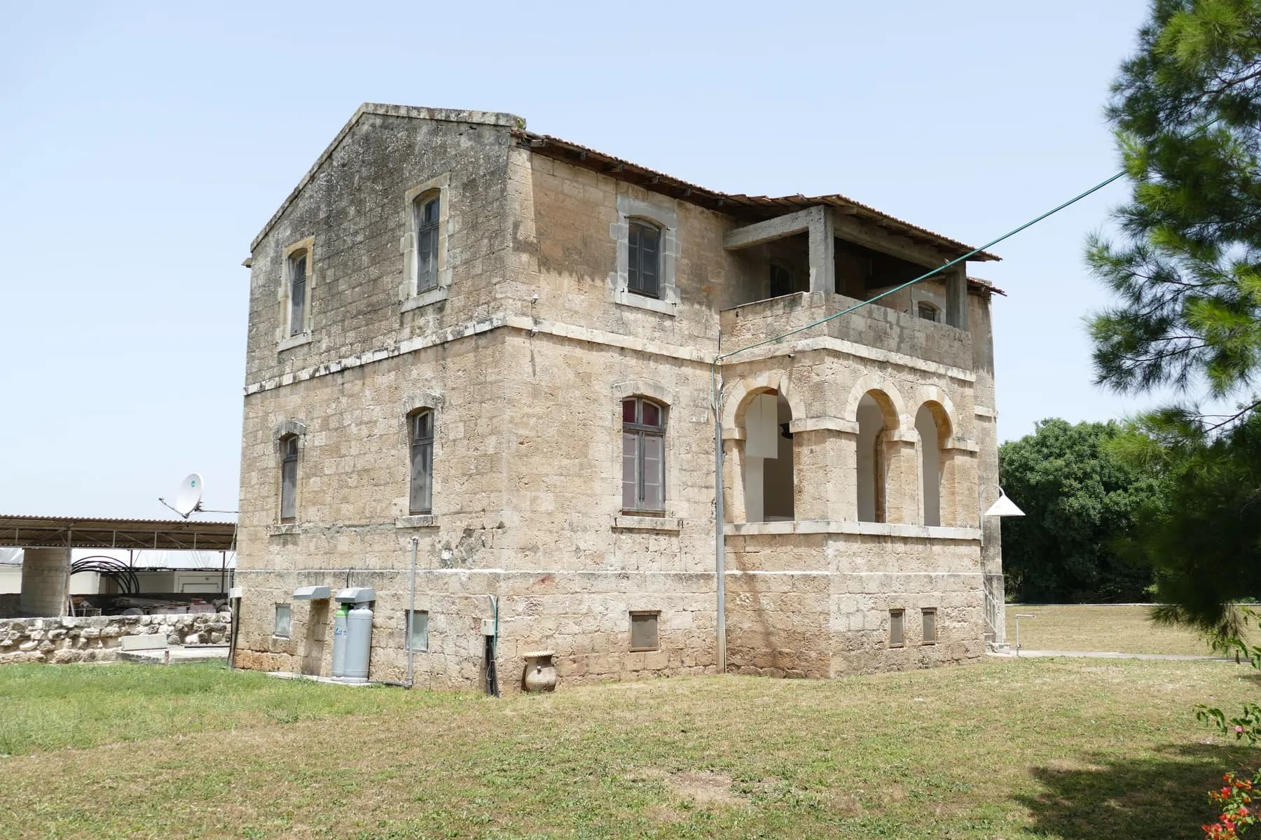 An old two-storey stone house in Bethlehem of Galilee, with an arched loggia on the ground floor and a covered balcony above it, standing on a lawn.