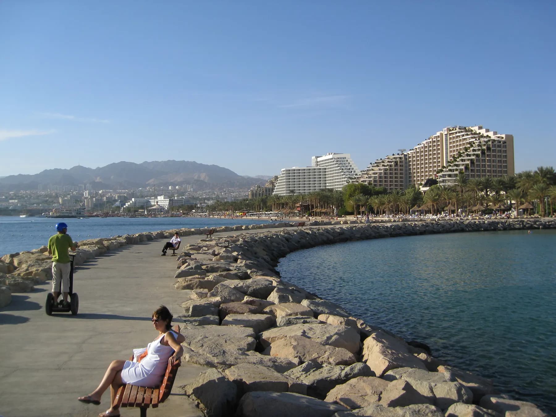 A walkway along the sea in Eilat, with terraced hotels and the red mountains behind