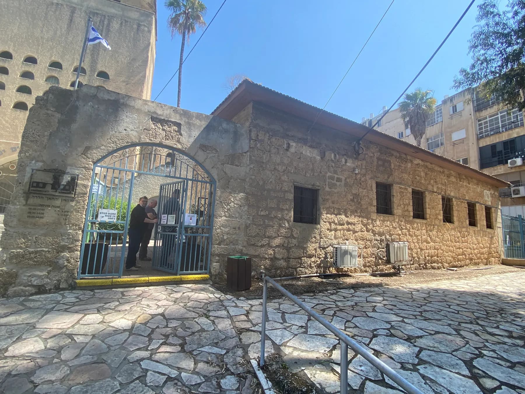The stone Khan of Hadera behind its iron gate, with the tower of the Great Synagogue beside it
