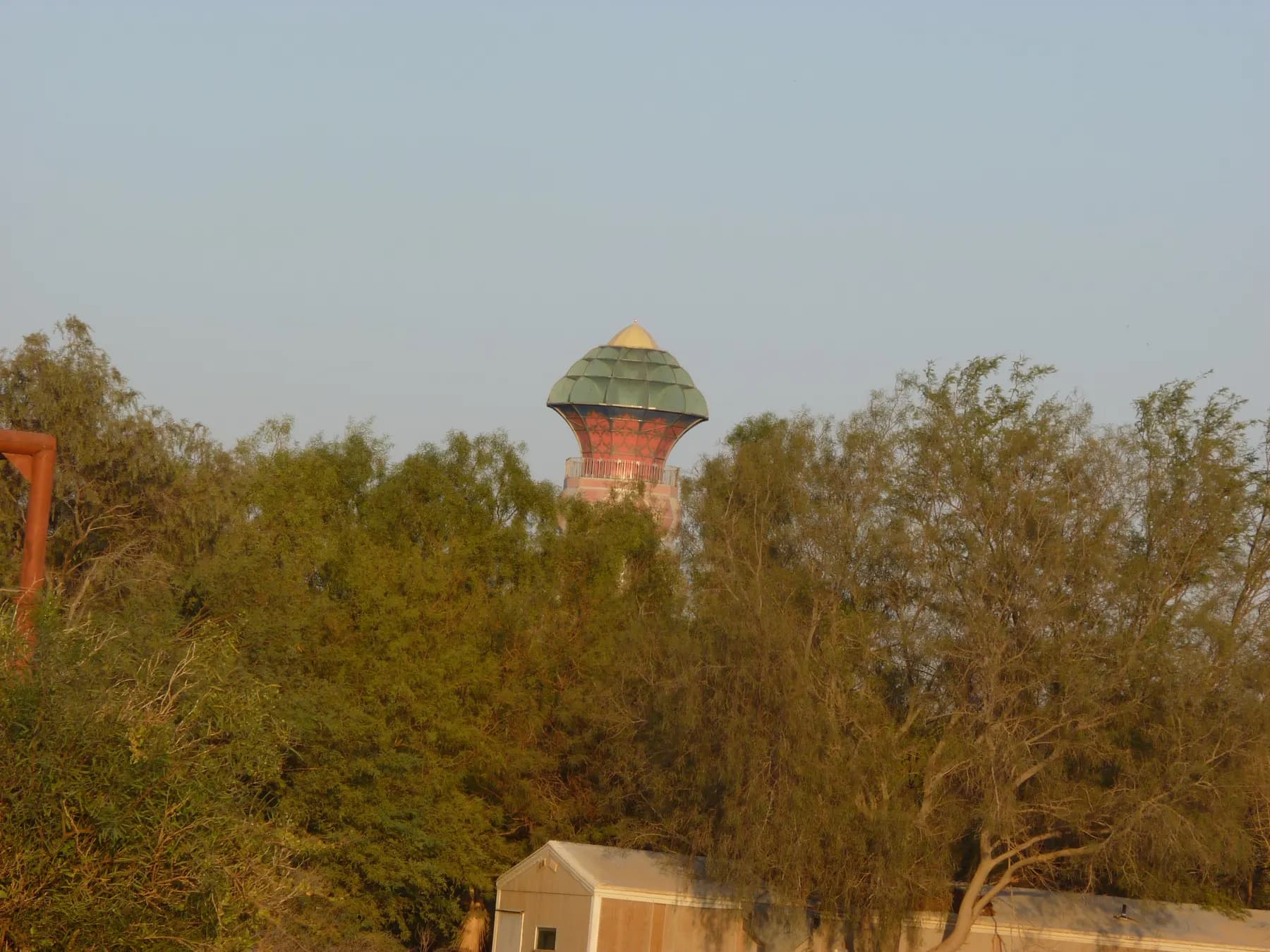 The tower of the Arts Building in Neot Semadar, with a red patterned shaft and a green domed top, rising above a line of trees.