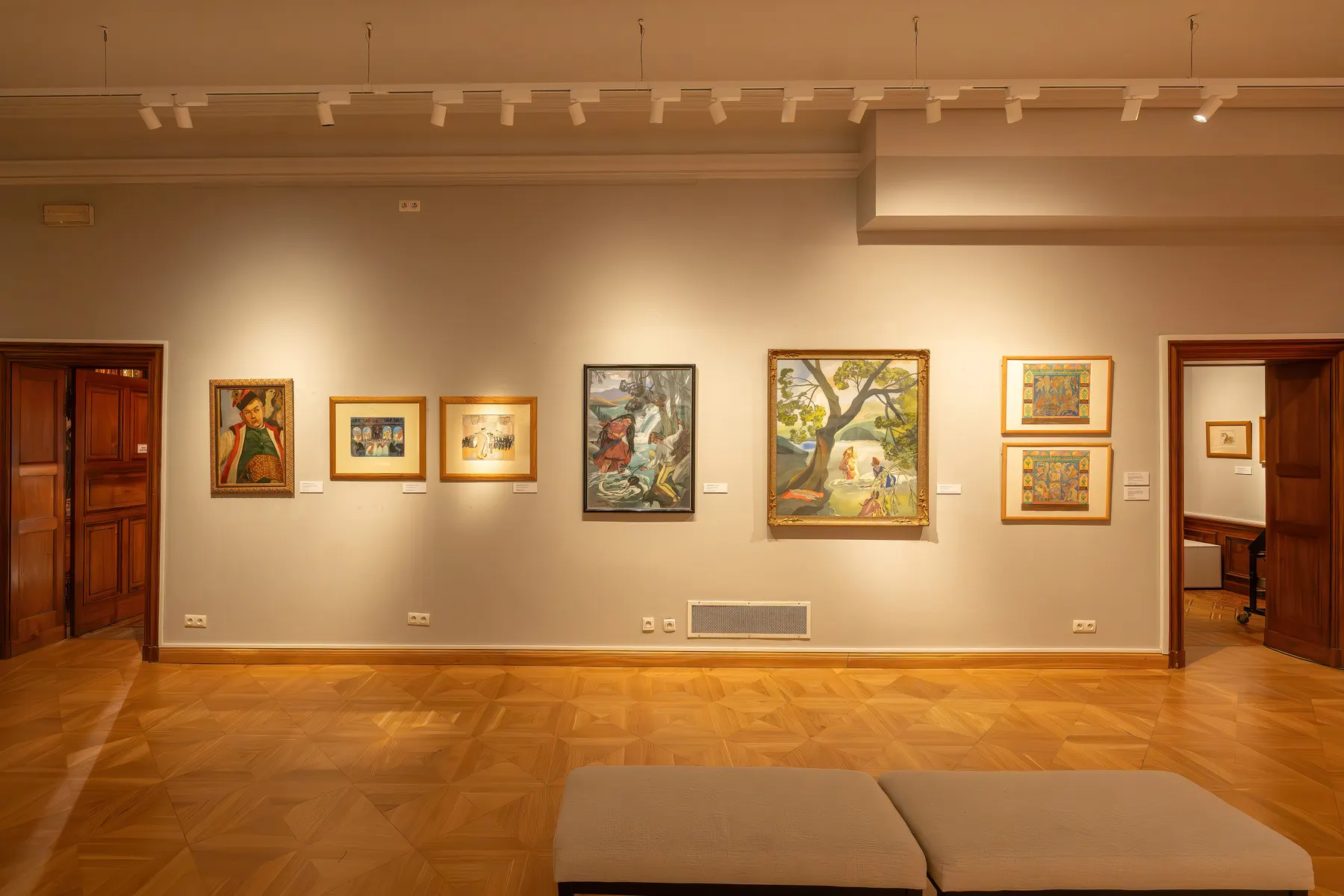 Framed paintings hung on the walls of a gallery room.