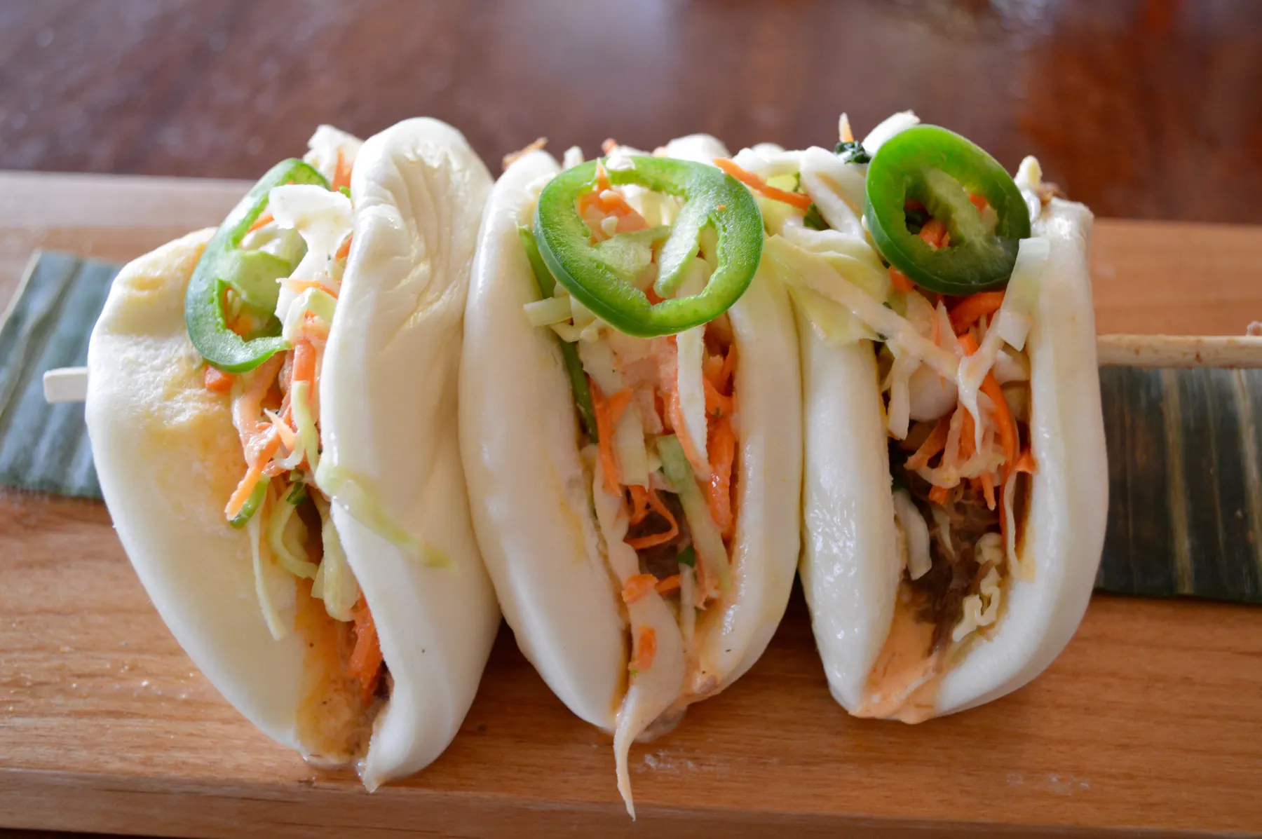 Three steamed bao buns filled with slaw and topped with sliced jalapeño