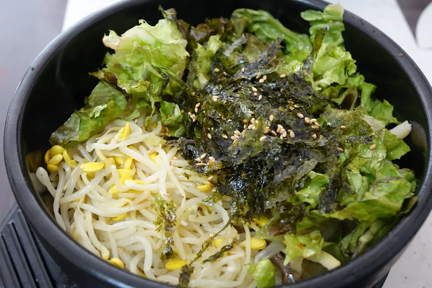 Bibimbap in a stone bowl, topped with lettuce, bean sprouts, seaweed and sesame