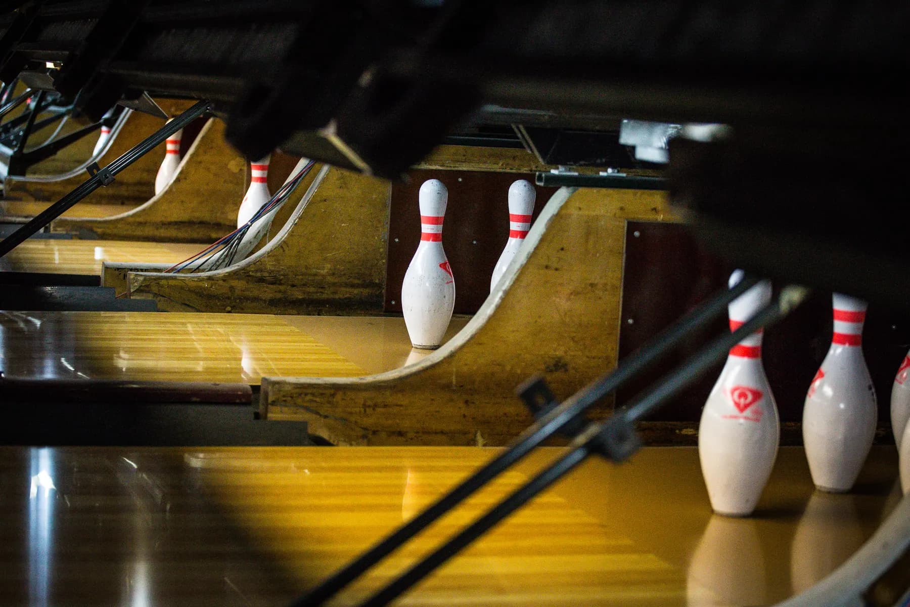 Bowling pins standing at the end of polished wooden lanes, with the pinsetter's sweep above them