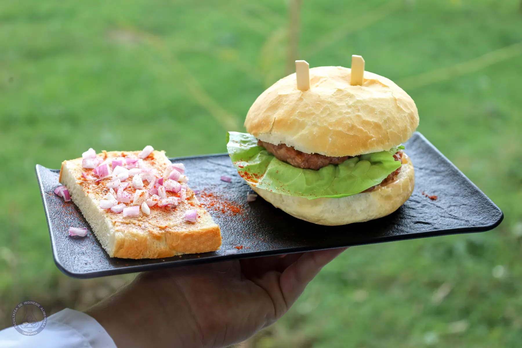 A beef burger with lettuce in a soft bun, served on a slate board.
