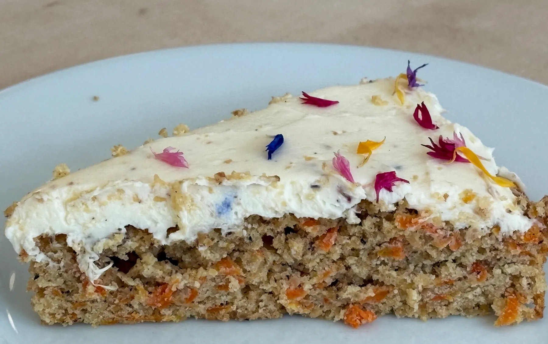 A slice of carrot cake with cream cheese frosting and flower petals