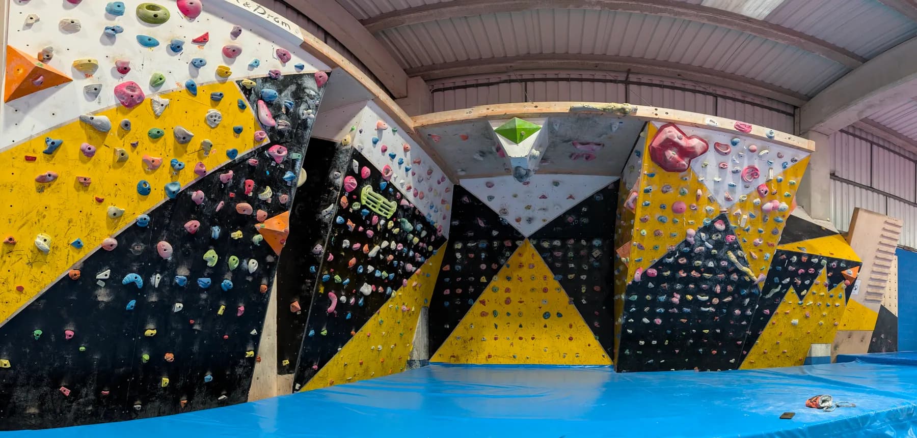 An indoor bouldering wall covered in coloured holds above a padded floor.