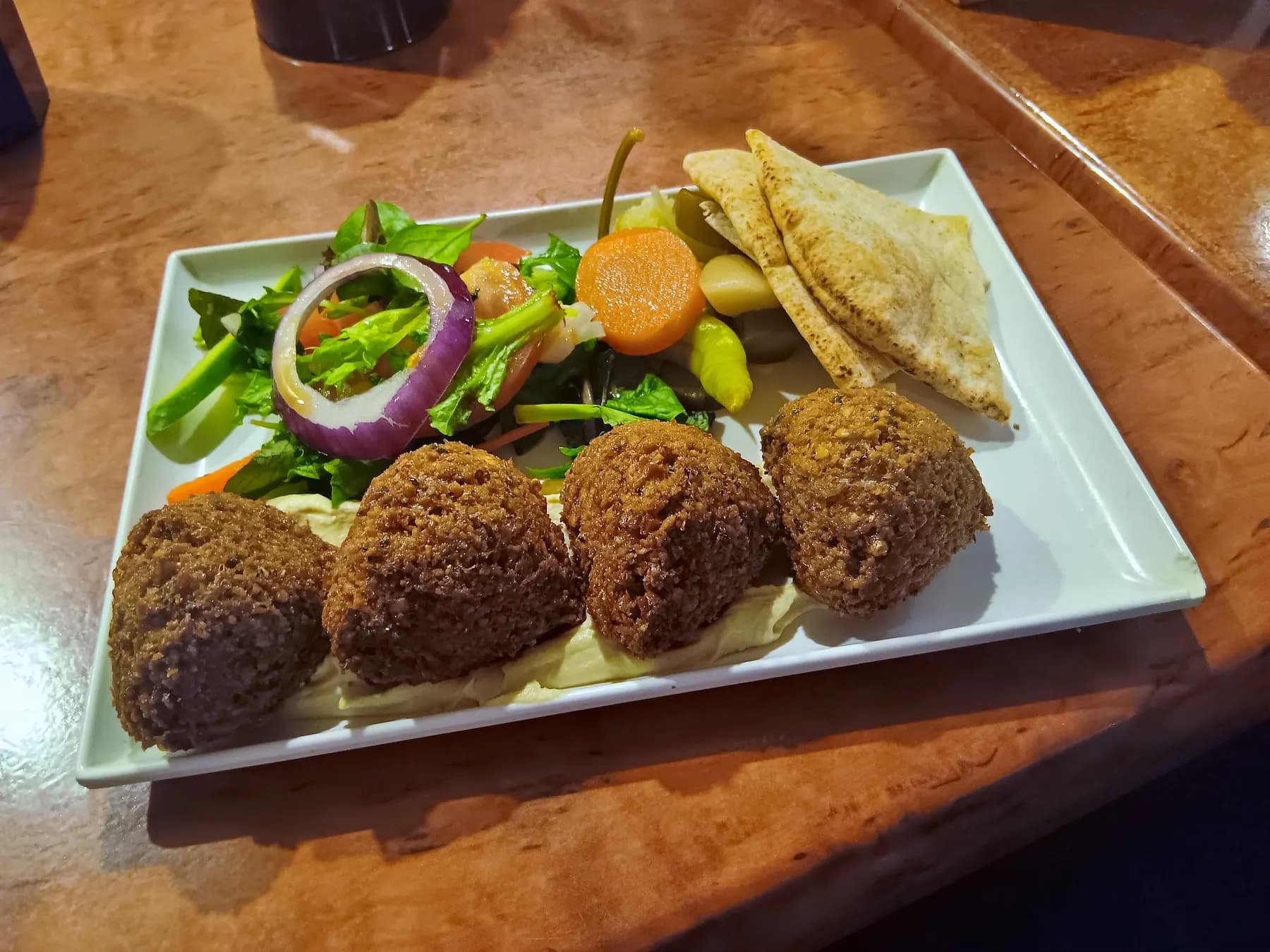Four falafel balls on a plate with salad, pickles and pita.