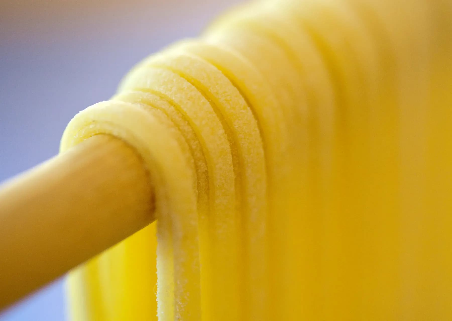 Strands of fresh pasta hanging over a wooden rod to dry