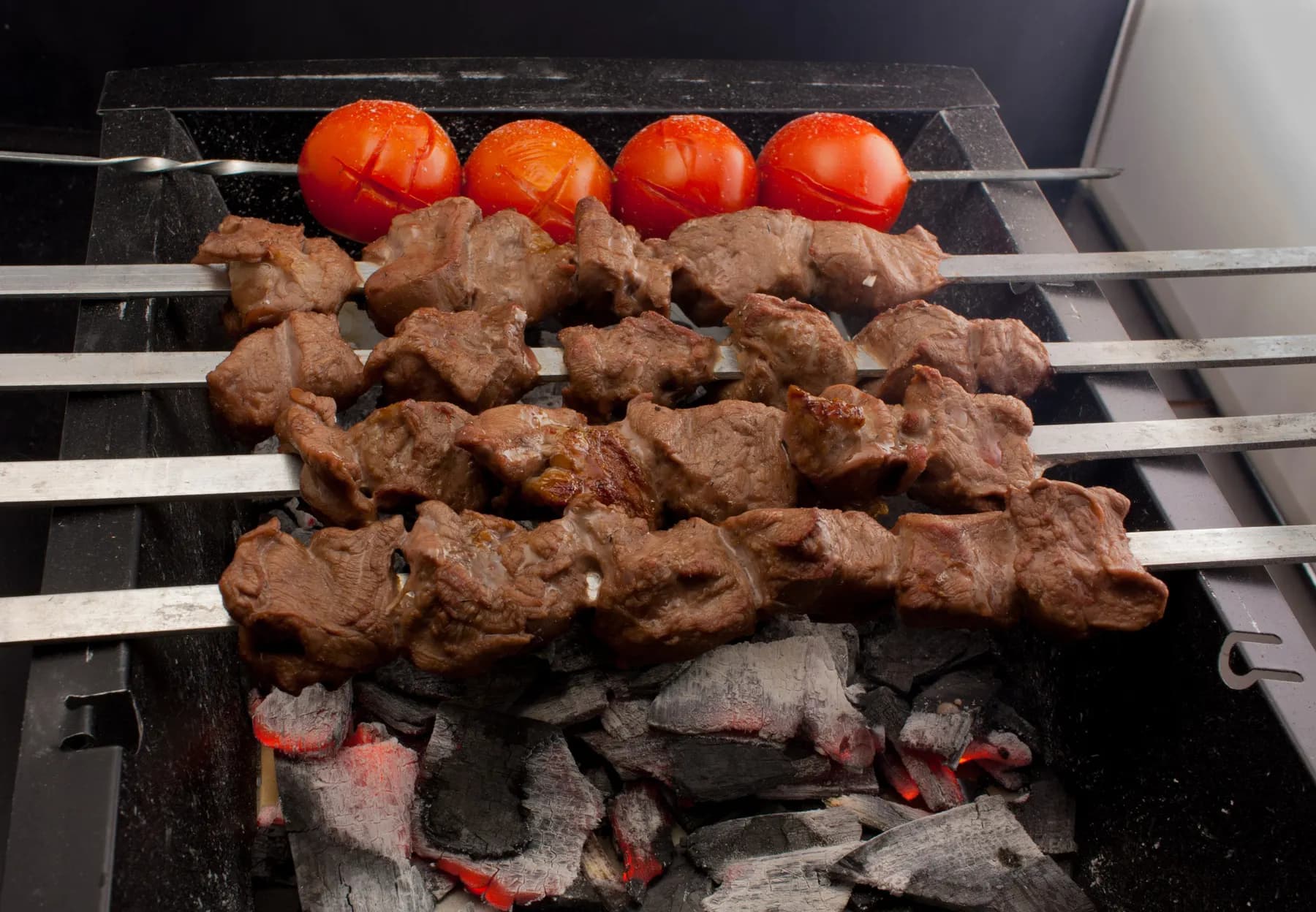 Skewers of lamb and whole tomatoes over glowing charcoal