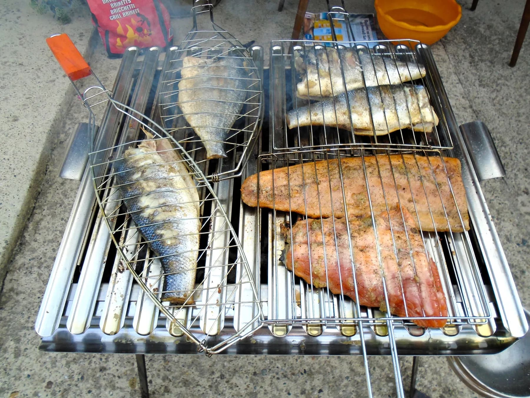 Whole fish and fish fillets in grill baskets over a charcoal grill