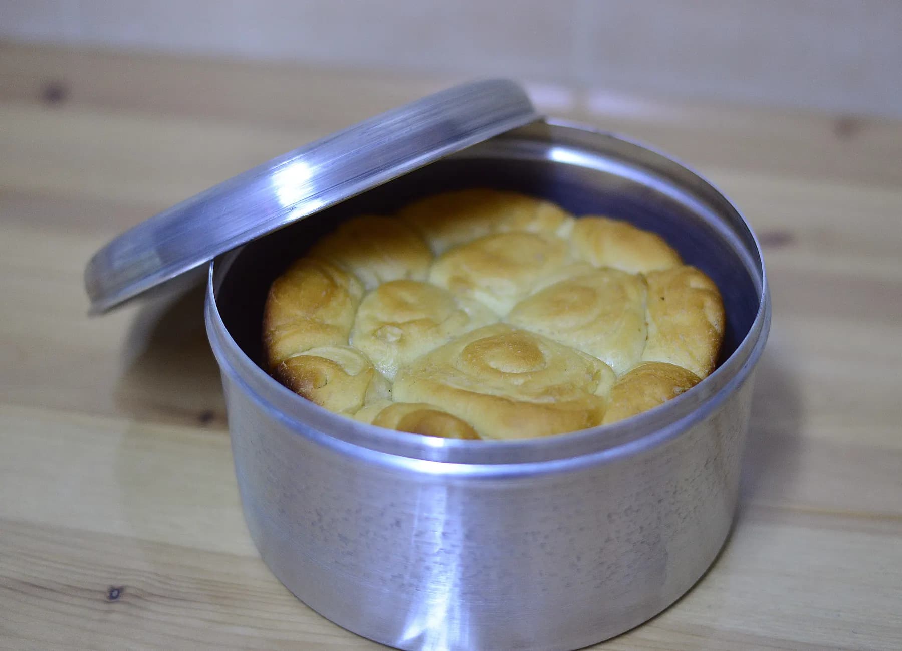 A round kubaneh loaf in its metal pot, the lid tilted open