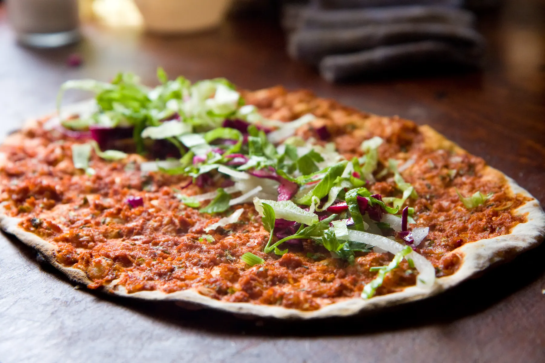 A spicy lahmajun, thin flatbread spread with minced meat, topped with shredded lettuce and sliced onion