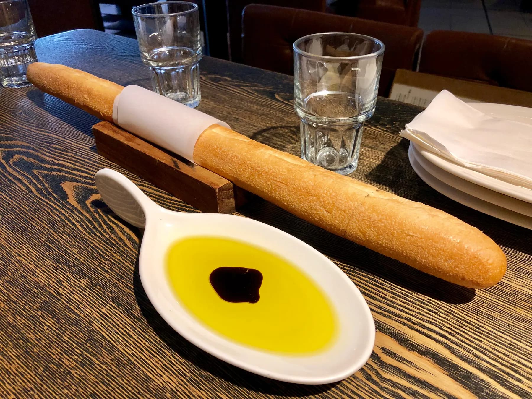 Olive oil with a drop of balsamic in a white dish, beside a baguette.