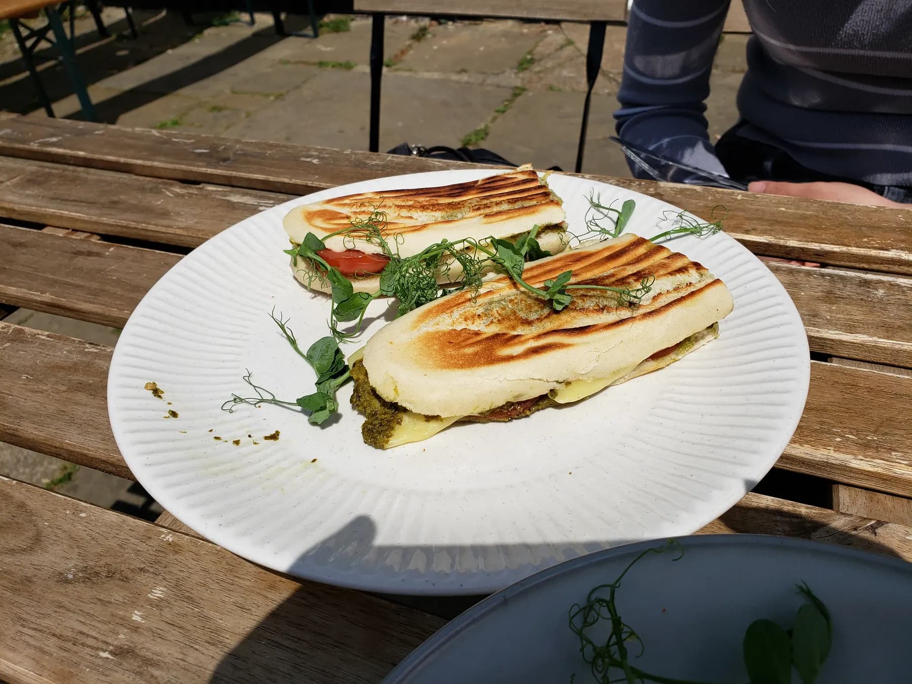 Two grilled panini of mozzarella, pesto and tomato on a white plate at an outdoor table