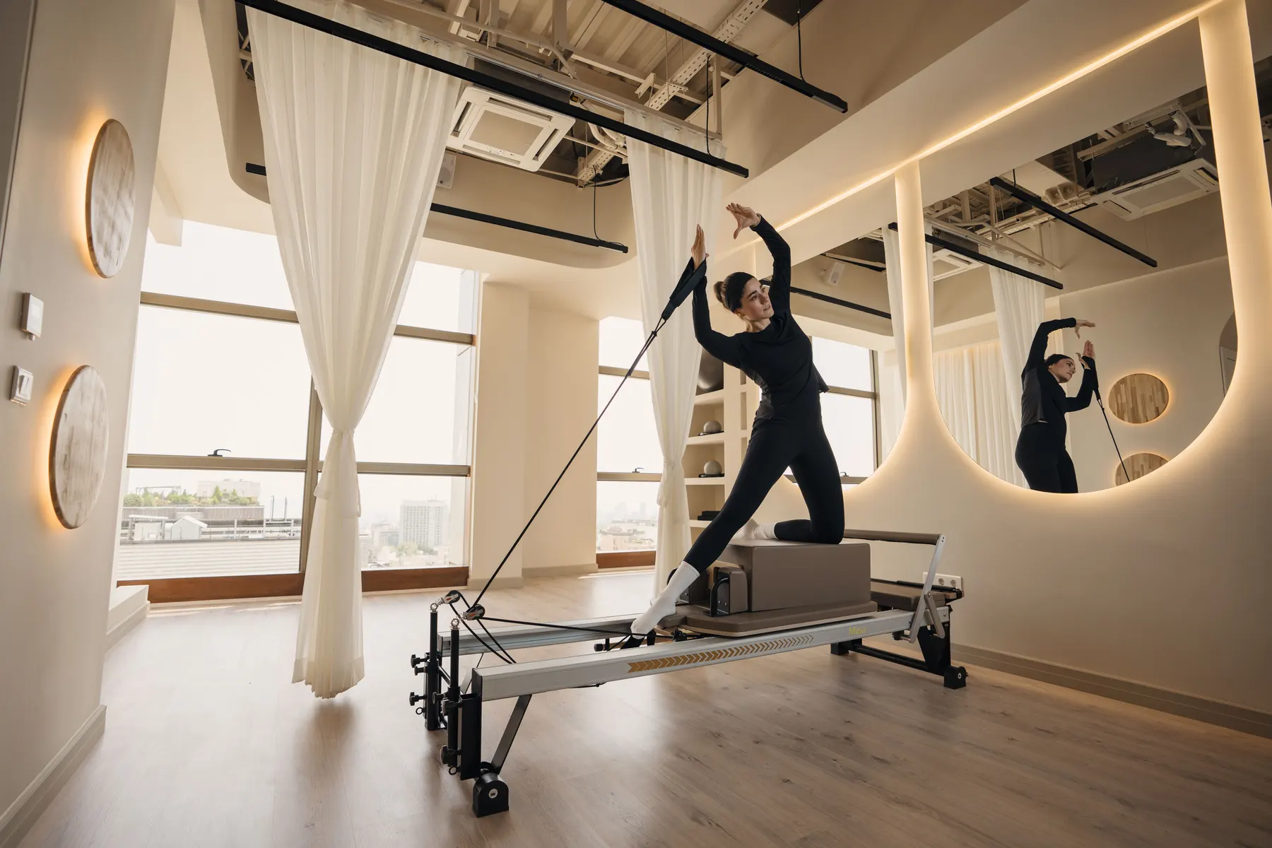 A Pilates reformer in a bright studio with curtains.
