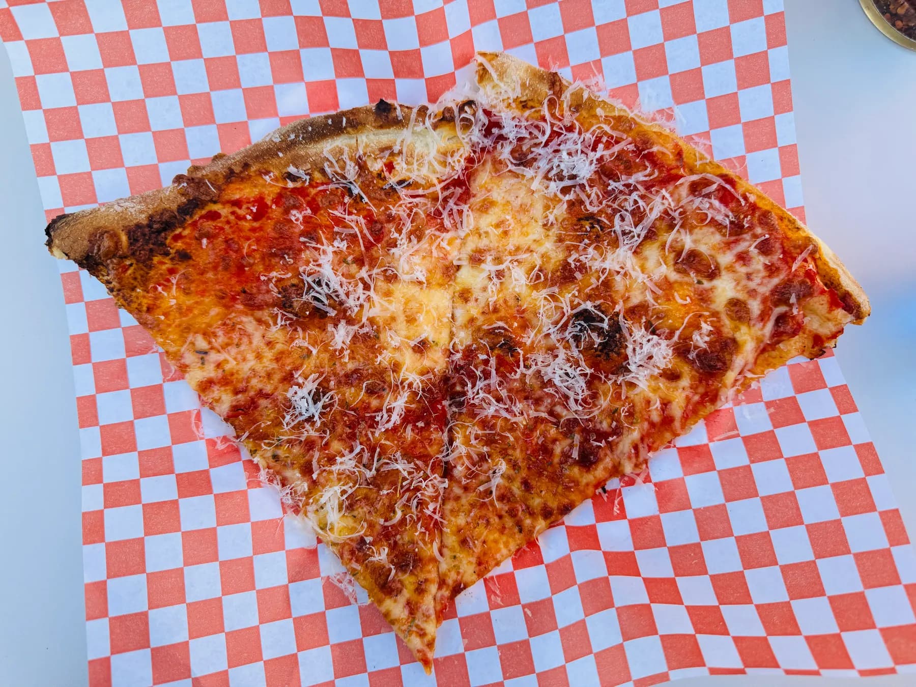 A wide slice of New York style cheese pizza on checked paper