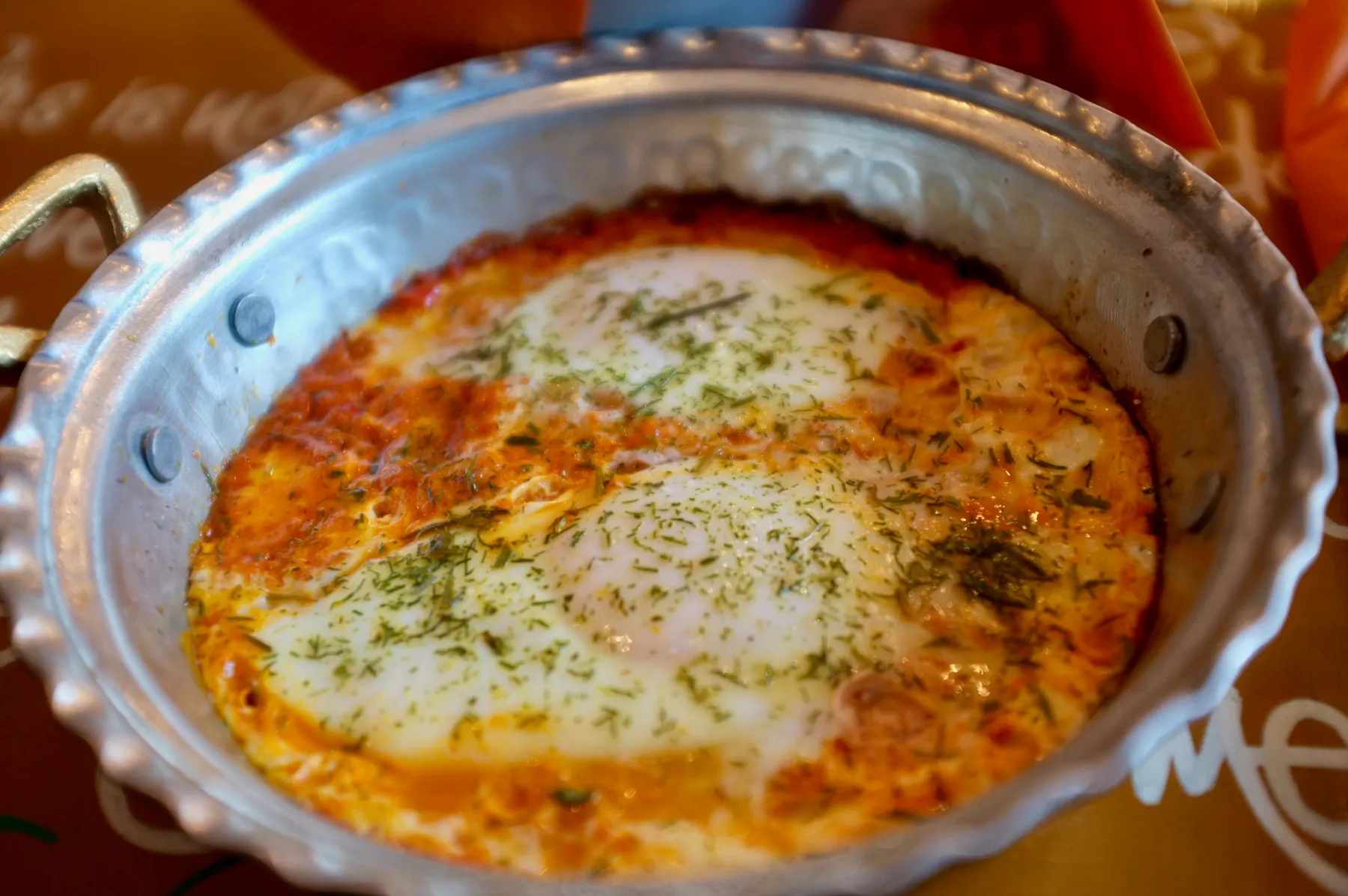 Shakshuka in a metal pan: eggs baked in tomato sauce, sprinkled with herbs