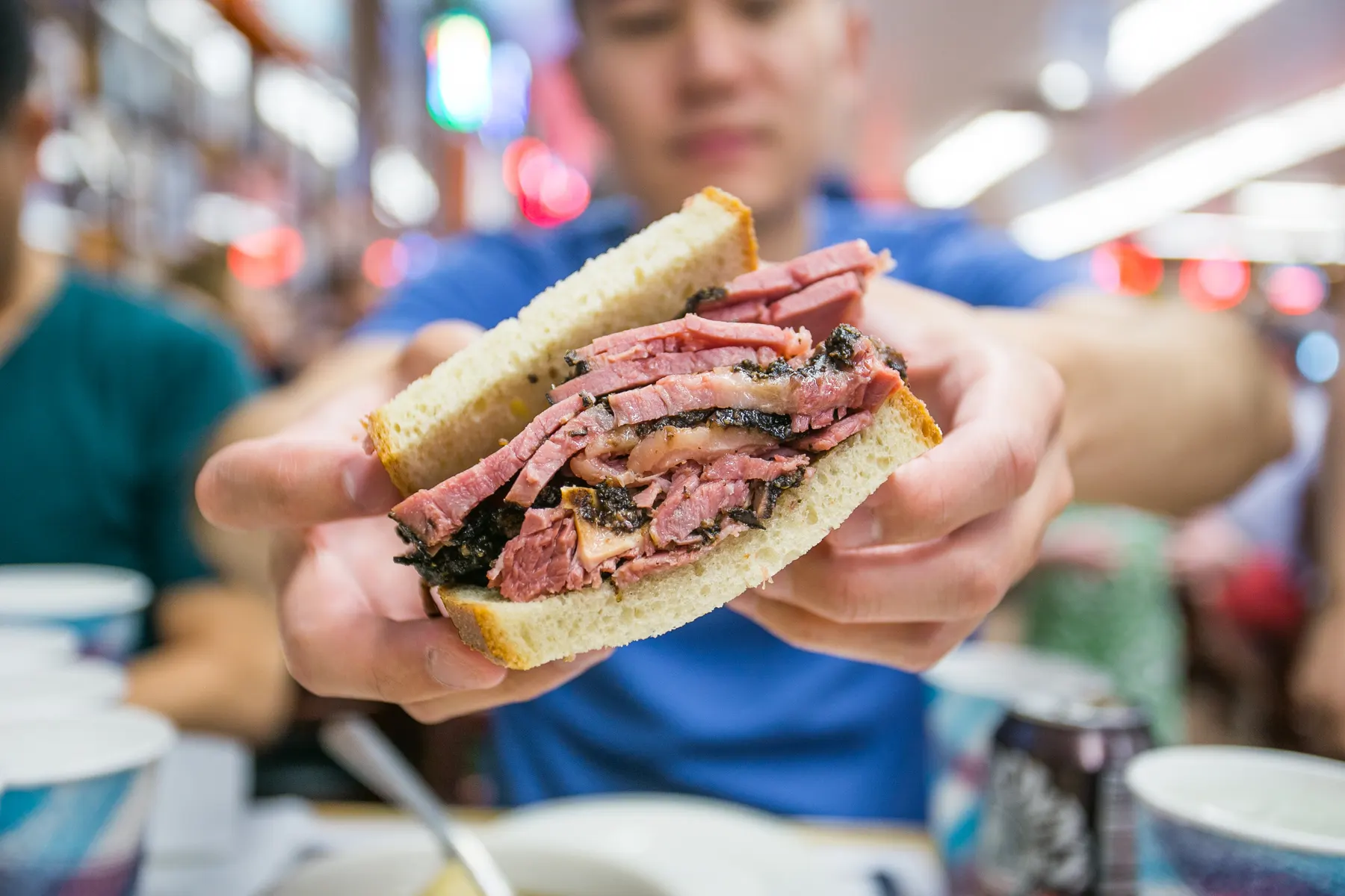 A pastrami sandwich piled high with hand-carved smoked meat, held up to the camera