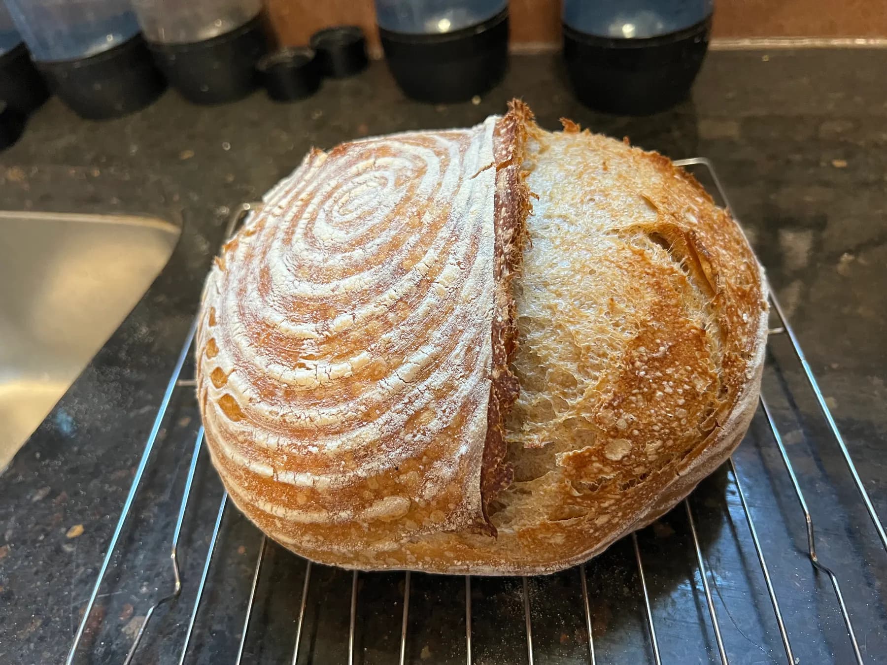 A round sourdough loaf dusted in a flour spiral, cut in half on a cooling rack