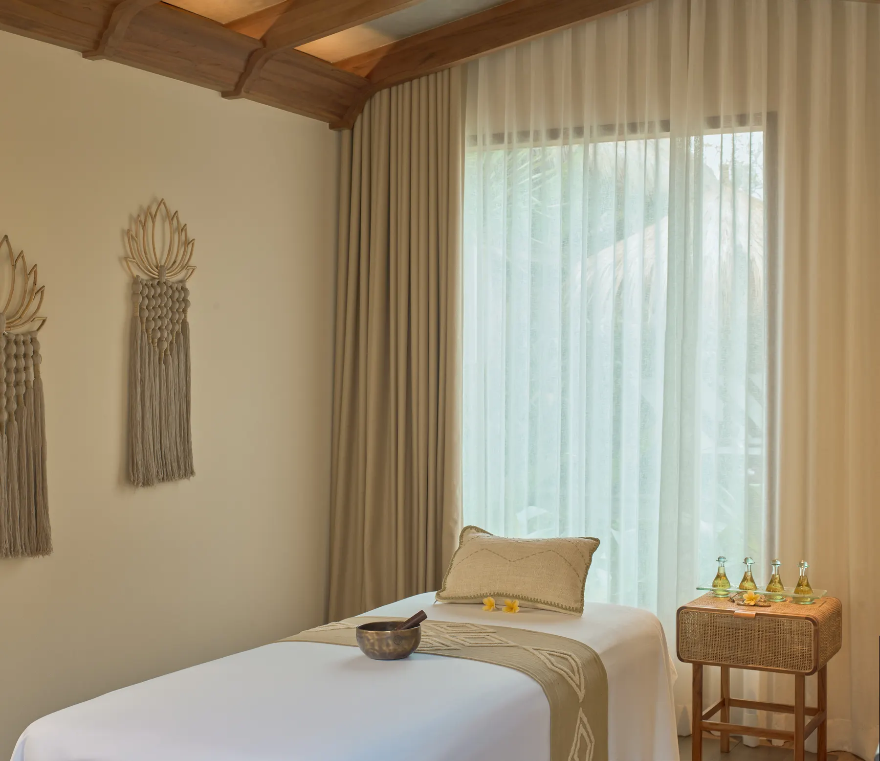 A spa treatment bed with oils and a singing bowl beside sheer curtains.