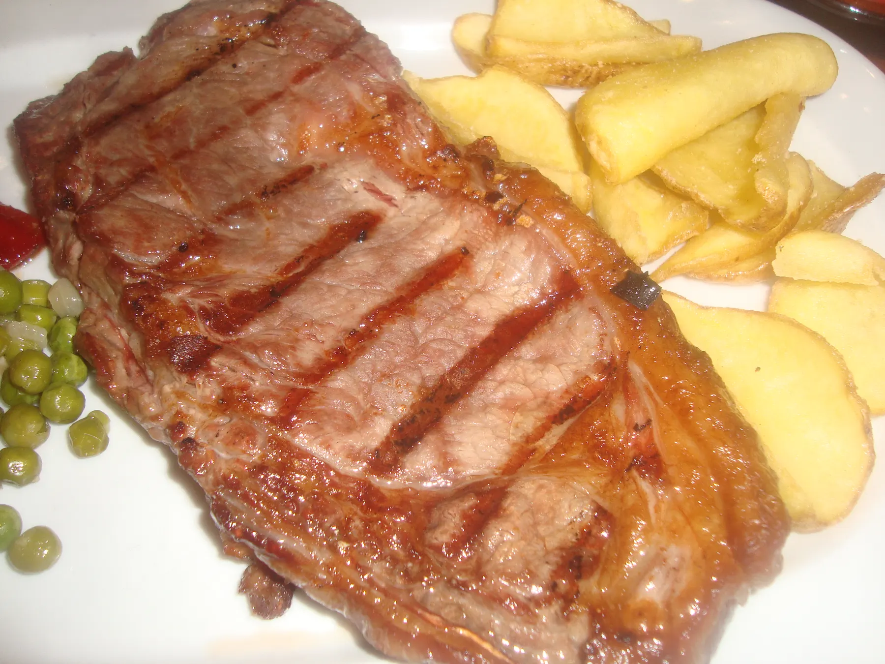 An entrecôte steak with grill marks from the coals, with chips and peas