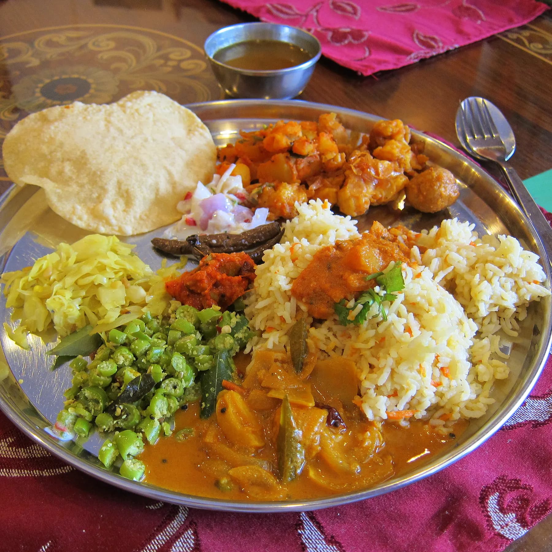 A vegan thali on a steel plate: rice, curries, vegetables and a papad
