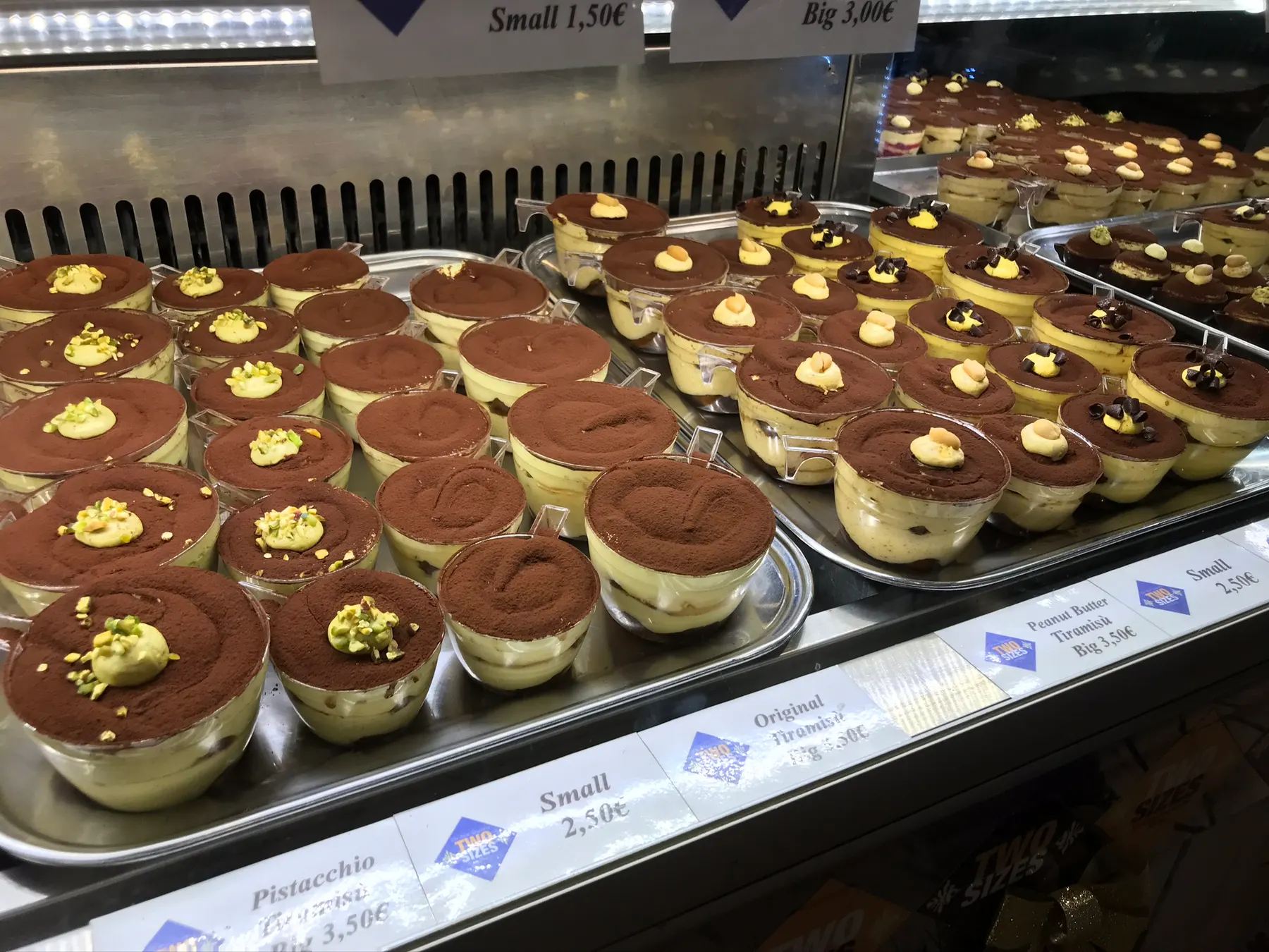 Cups of tiramisu dusted with cocoa in a shop's chilled counter, priced by size