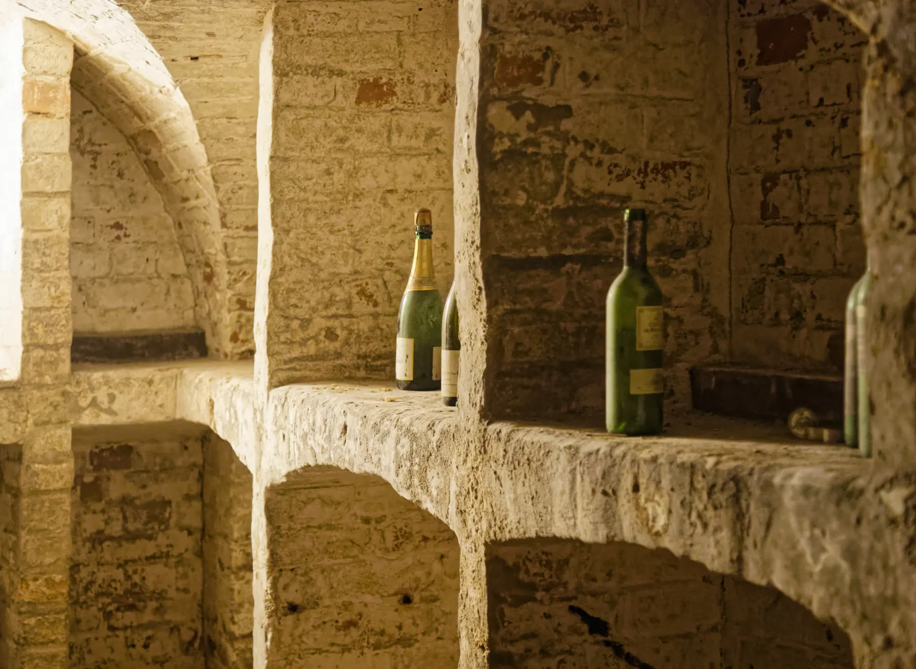 Wine bottles resting in the stone arches of an old cellar